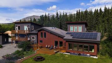 A modern log cabin with a deck, large windows, and solar panels.