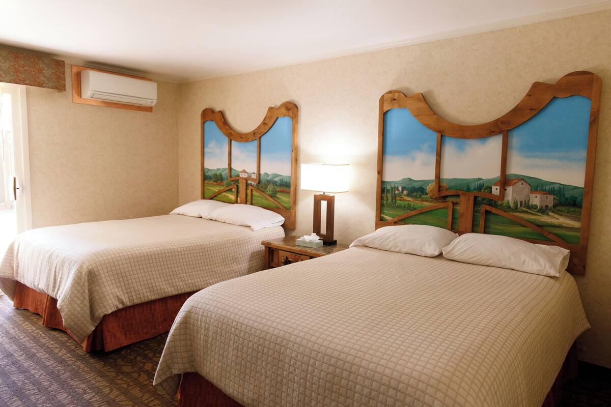 A hotel room with two beds, a nightstand, a lamp, and a painting of a landscape on the wall.