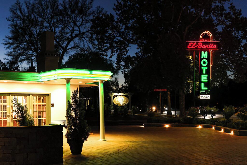 A motel with a neon sign, a gas station, and a paved entrance area.