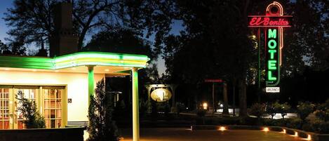 A motel with a neon sign, a gas station, and a paved entrance area.