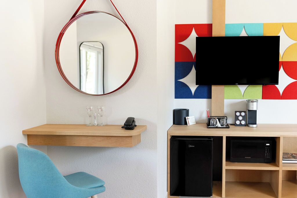 Une chambre d’hôtel moderne équipée d’un bureau en bois, d’un petit réfrigérateur, d’un four à micro-ondes, d’une machine à café et d’un téléviseur à écran plat.