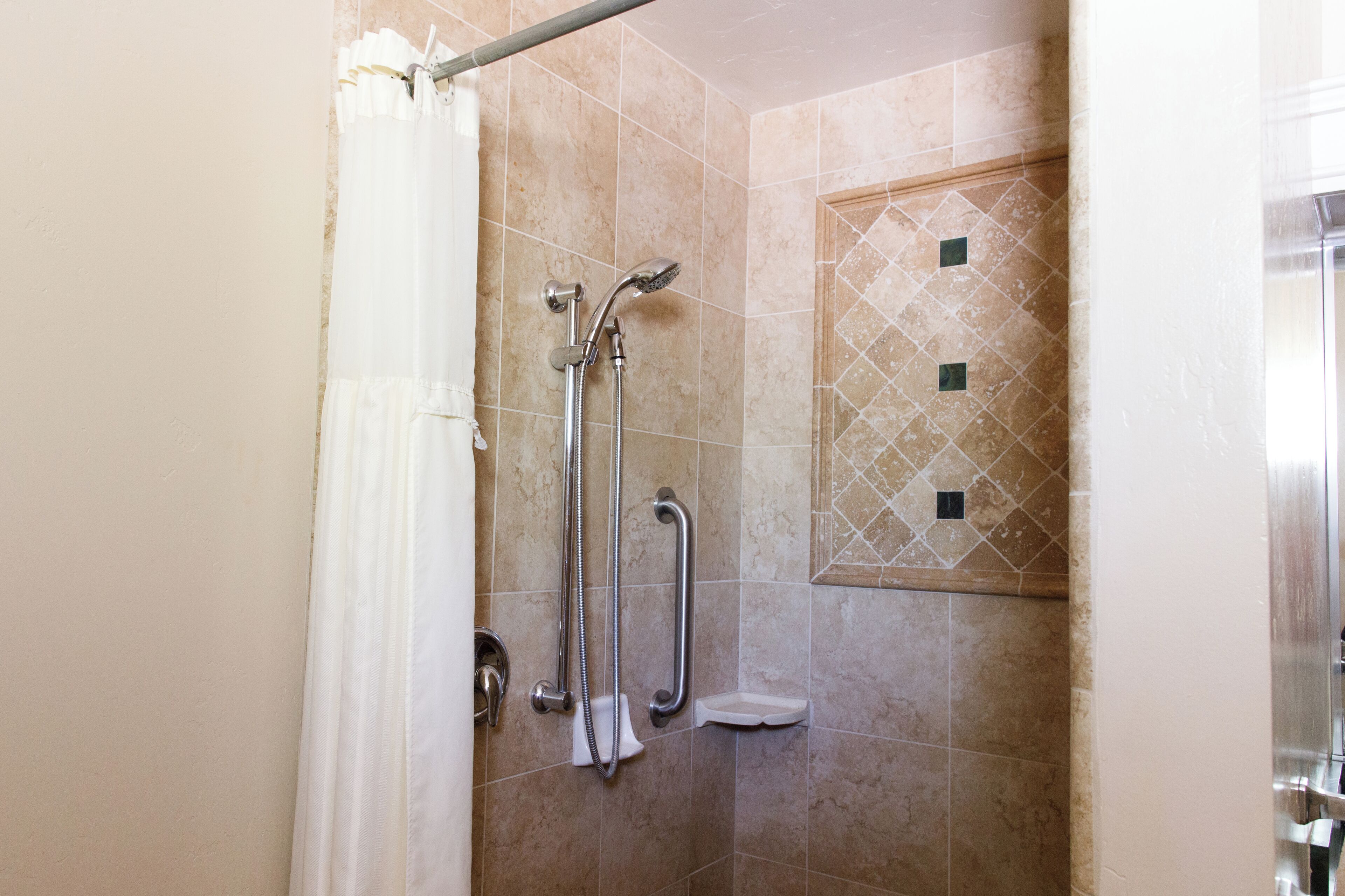 Ducha con barra de apoyo, cabezal de ducha manual y toallero blanco.