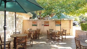 An outdoor patio with wooden tables and chairs, a green umbrella, and artwork on the wall.
