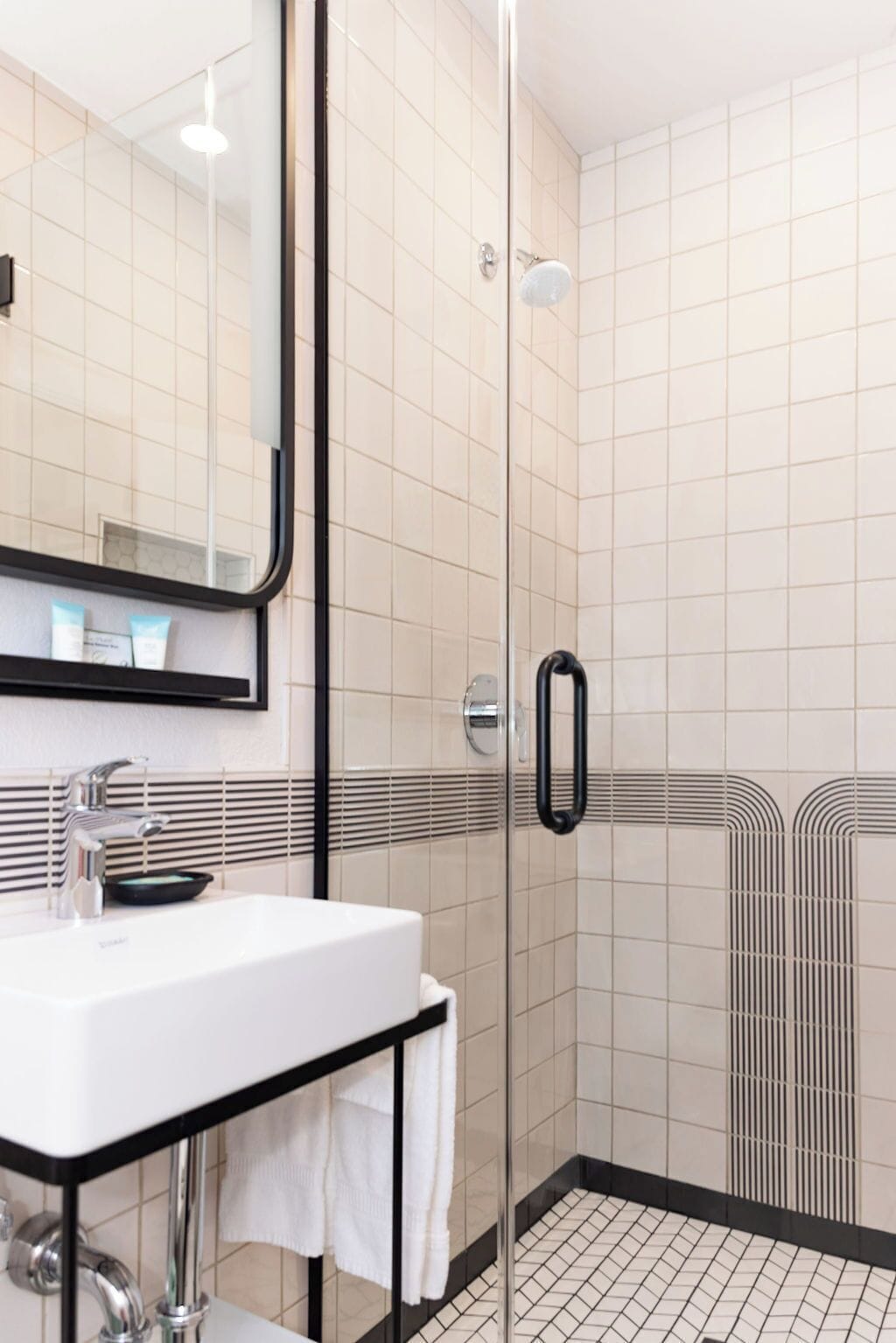 A modern bathroom with a glass shower enclosure, a white sink with a black countertop, and a large mirror.