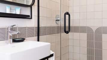 A modern bathroom with a glass shower enclosure, a white sink with a black countertop, and a large mirror.