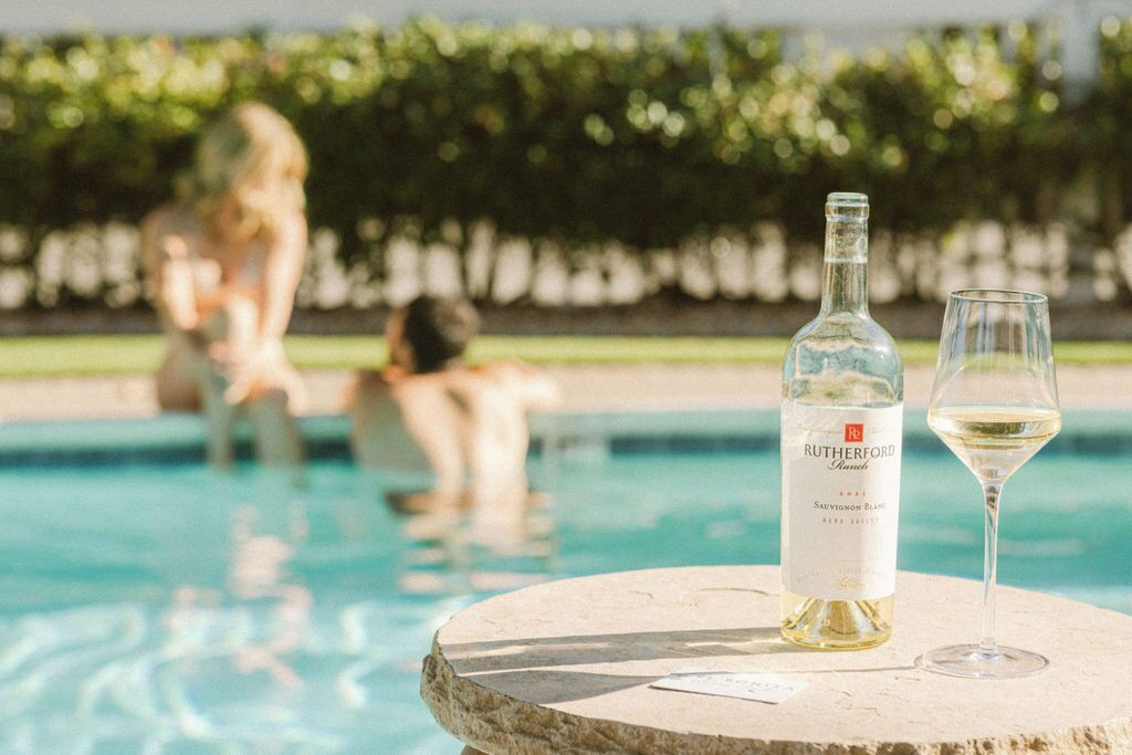 A bottle of Rutherford Wines Sauvignon Blanc and a glass on a stone table by a pool.