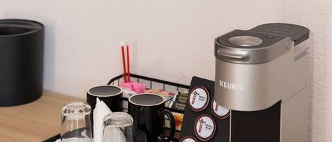 A coffee maker with multiple coffee pod options, a tray with cups and a spoon, and a mirror reflecting a hotel room.