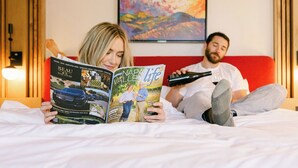Two people lying on a bed, one reading a magazine and the other holding a bottle.
