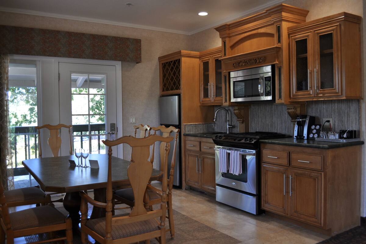 A kitchen with wooden cabinets, stainless steel appliances, and a dining area with a table and chairs.