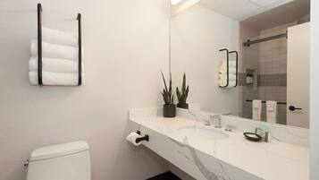 Un baño con inodoro blanco, lavamanos de mármol, toallero, espejo y planta en maceta.