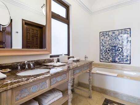 A bathroom with a marble vanity, two sinks, a large mirror, a towel rack, and a decorative blue tile backsplash.