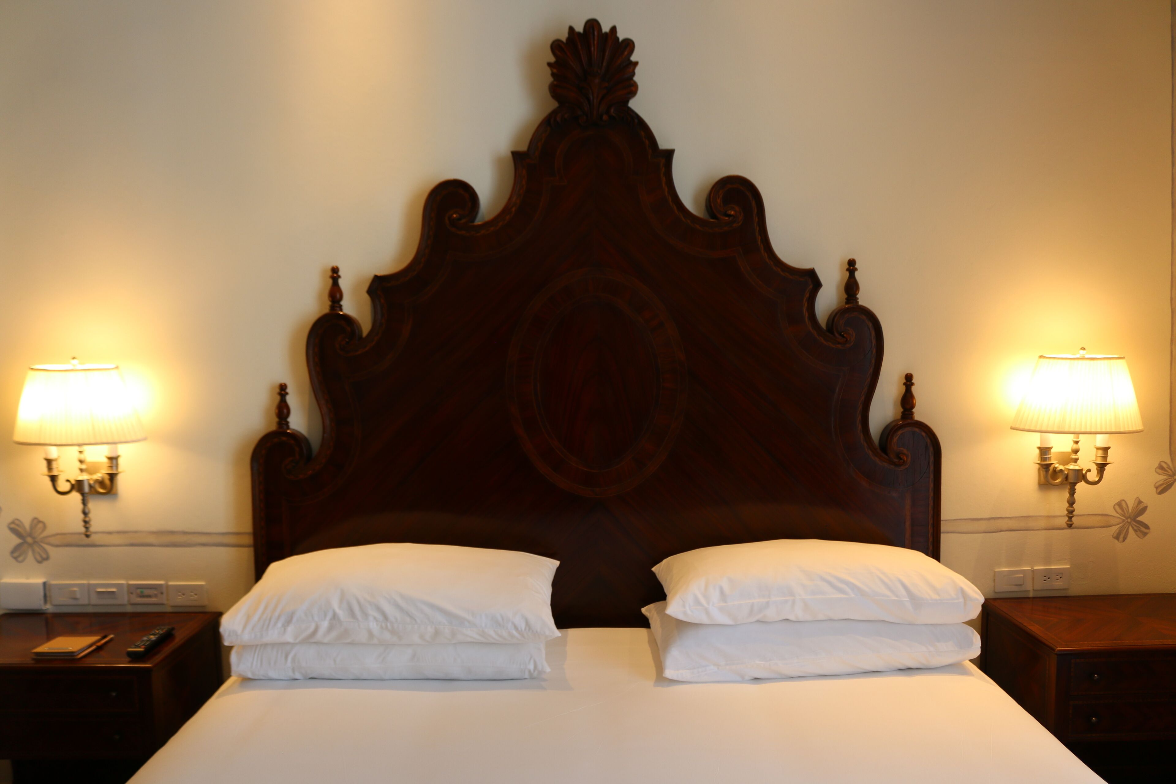 Una cama bien hecha con cabecera de madera, dos lámparas de noche y una mesita de noche con un control remoto.