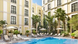 Pátio de hotel com piscina, espreguiçadeiras e palmeiras.