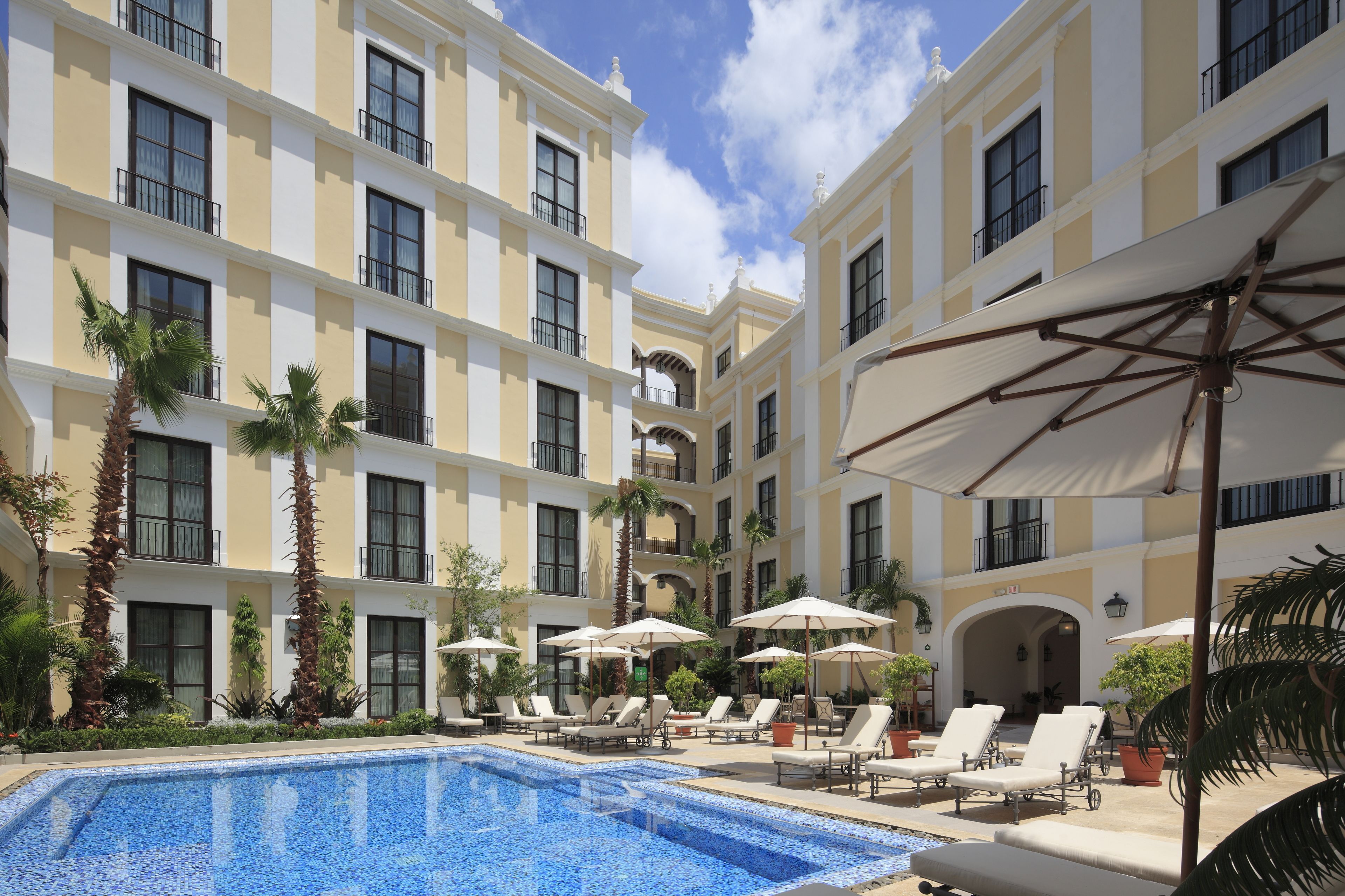 Un patio de hotel con piscina, tumbonas, sombrillas y palmeras.