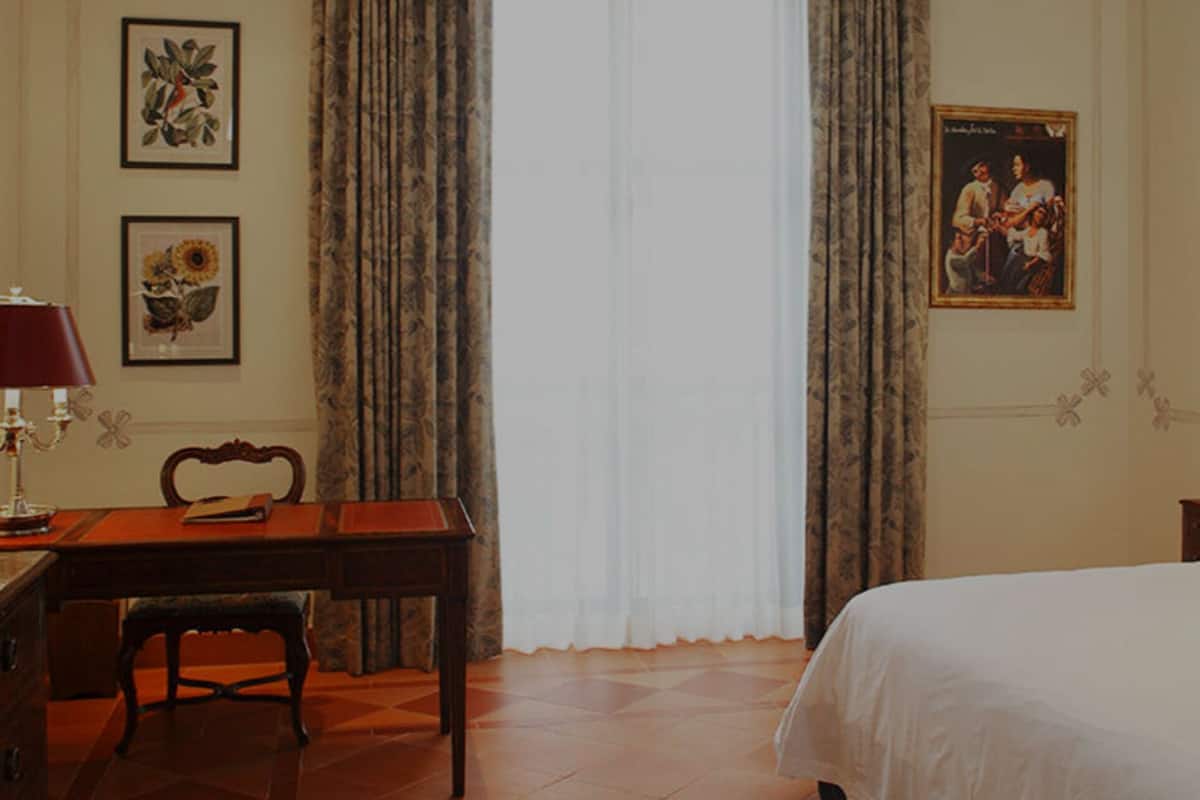 Una habitación de hotel con una cama de madera, un escritorio con lámpara, una silla y dos cuadros en la pared.