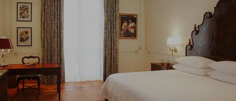 A hotel room with a wooden bed, a desk with a lamp, a chair, and two framed pictures on the wall.