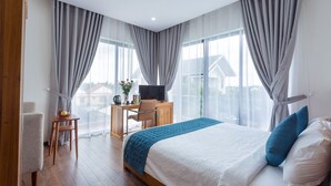 Een hotelkamer met een bed, bureau, stoel en uitzicht op gebouwen door grote ramen.