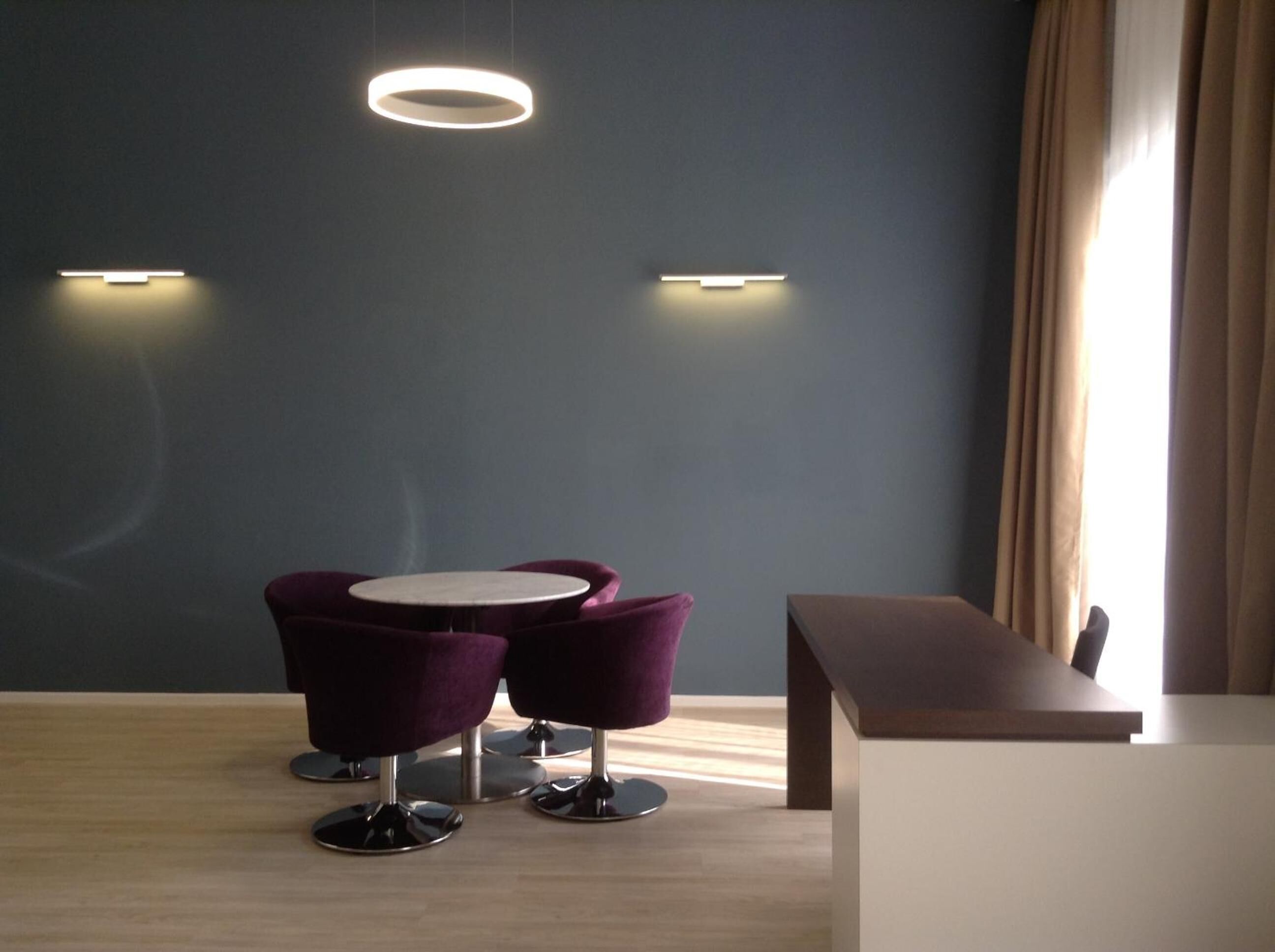A modern room with two purple chairs around a small table, a bench, and a circular light fixture on the wall.