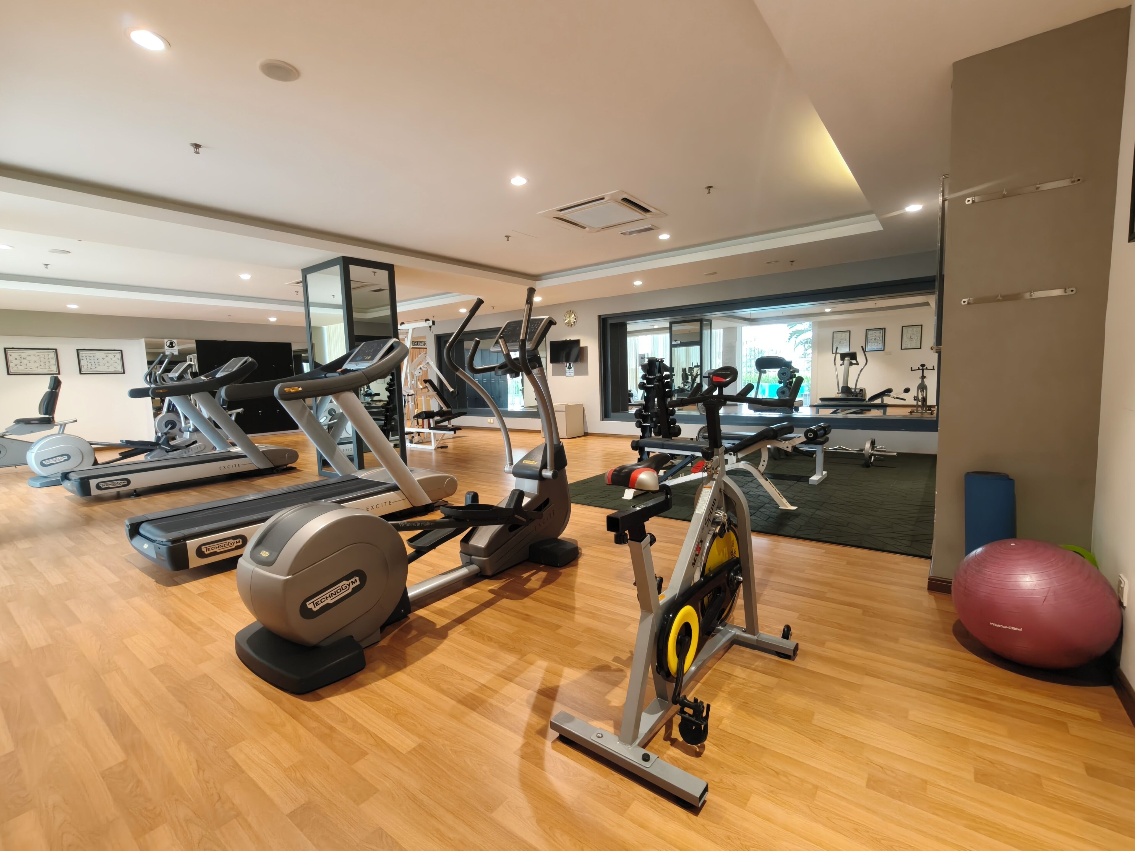 A gym with various exercise machines, a mirrored wall, and a wooden floor.