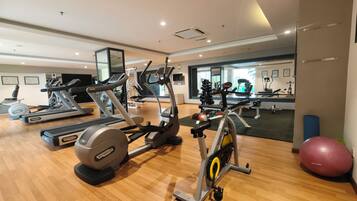 Un gimnasio con diversas máquinas de ejercicio, un espejo grande en la pared y suelo de madera.