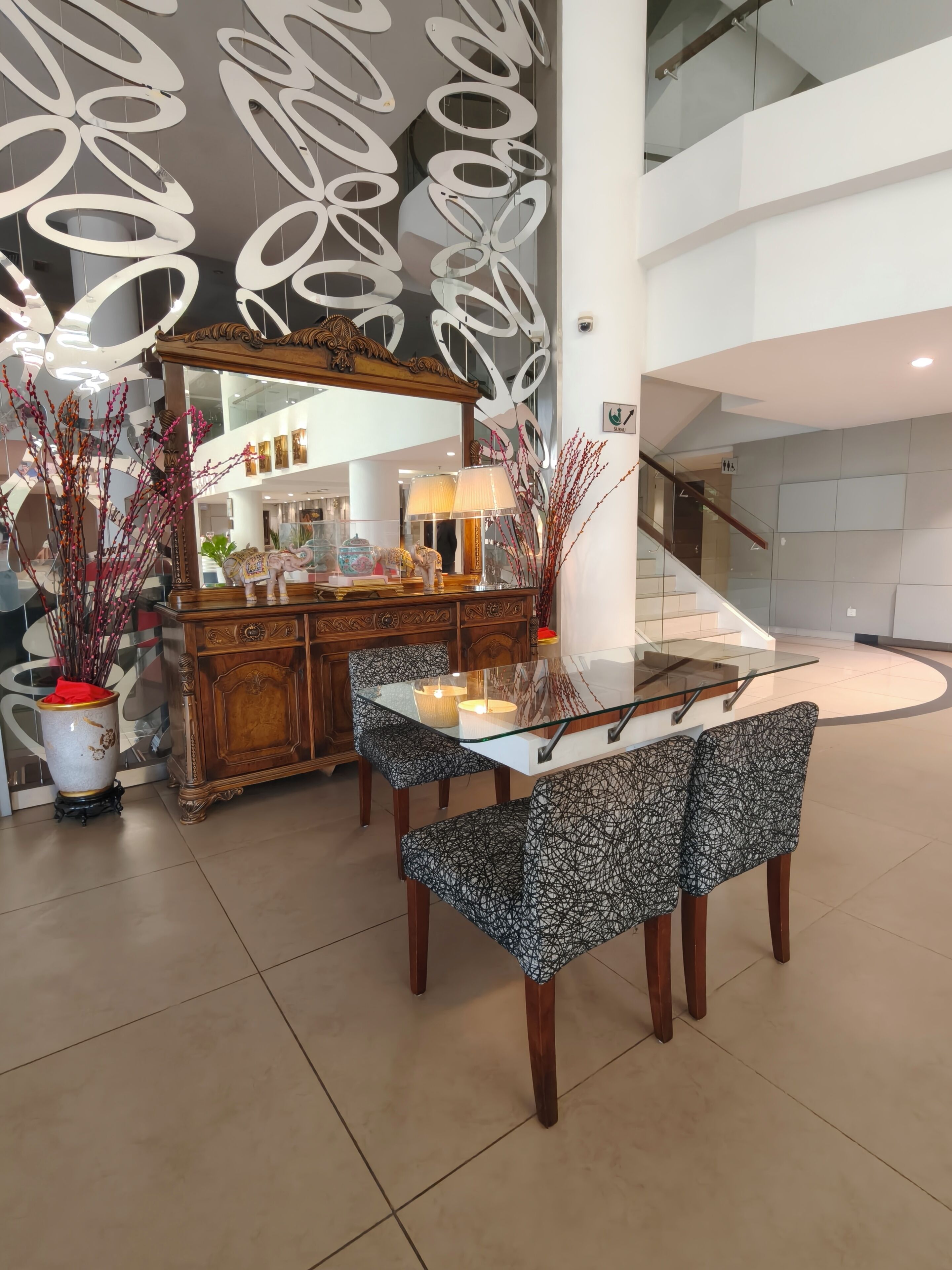 A modern dining area with a glass table, patterned chairs, a wooden cabinet, and decorative branches.
