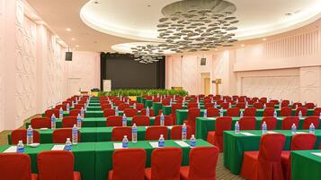 Ein Konferenzraum mit Tischen, Stühlen in Reihen, einer Bühne und einer großen Chandelier.