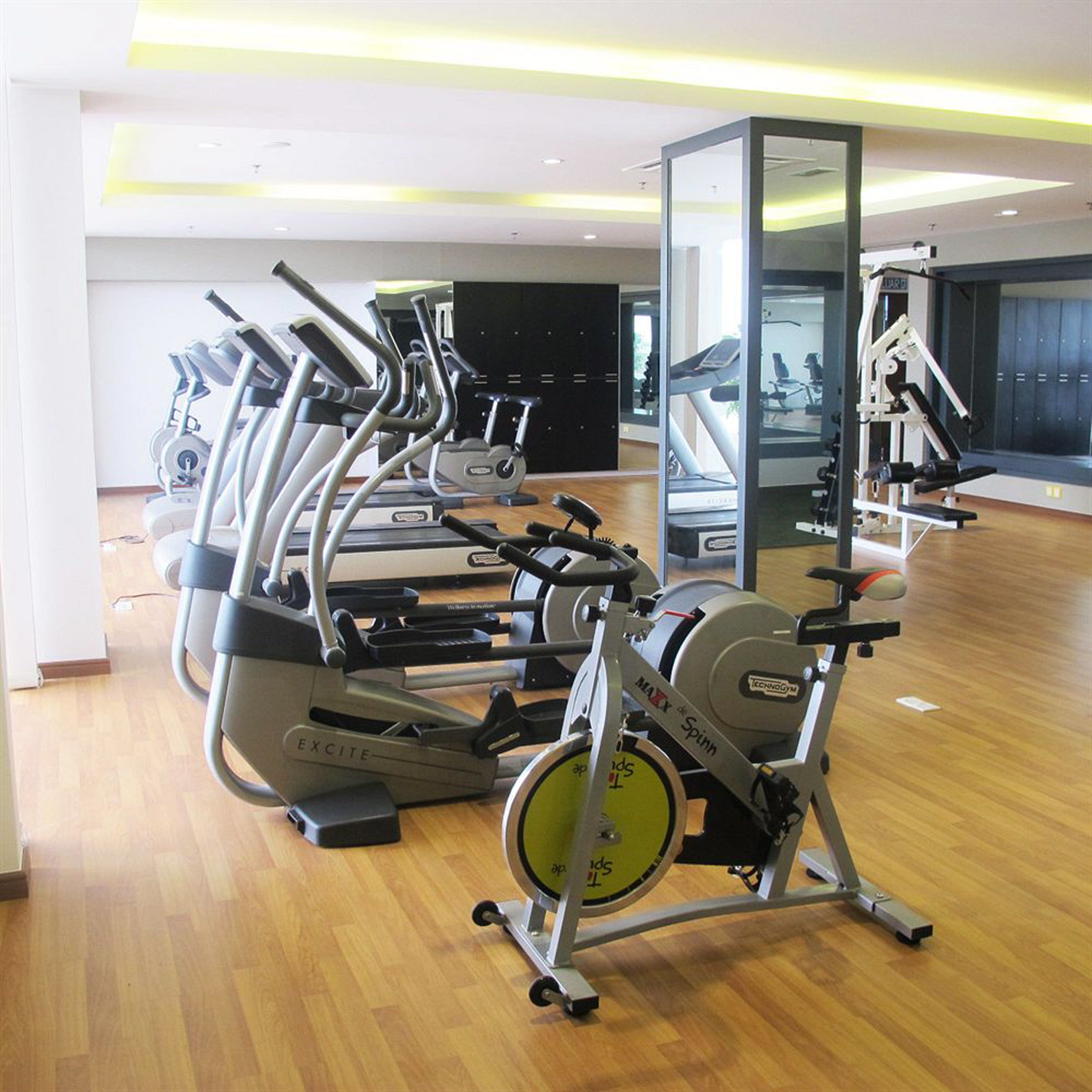 Un gimnasio con máquinas de cardio, un espejo grande y suelo de madera.
