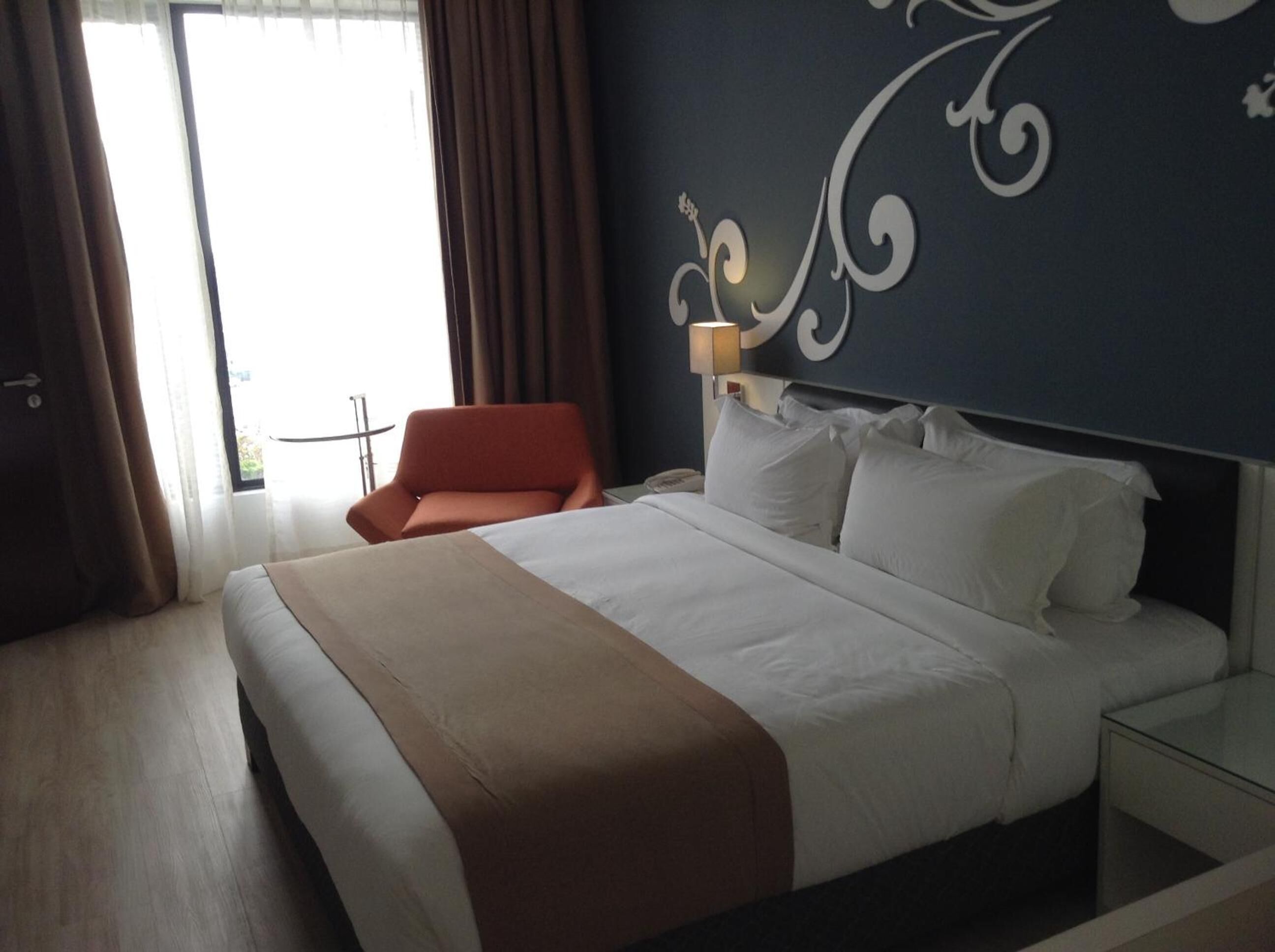 Una habitación de hotel con una cama grande, una silla, una mesita de noche y un adorno en la pared.
