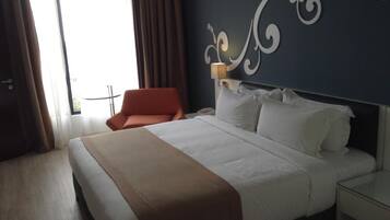 Una habitación de hotel con una cama grande, una silla, una mesita de noche y un adorno en la pared.