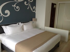 Een net opgemaakt bed met witte lakens en een beige plaid, een muur met een decoratief spiraalpatroon en een gesloten deur.