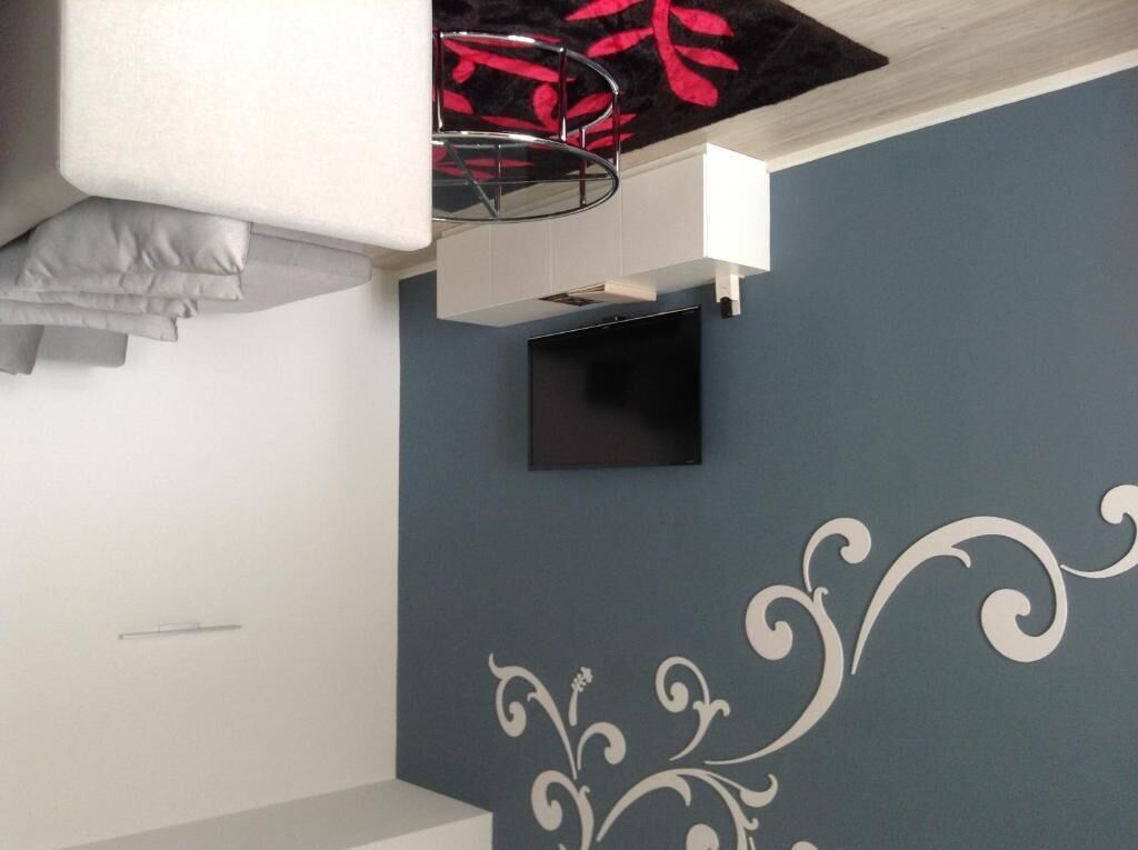 A room with a blue wall, a white decorative pattern, a flat-screen TV mounted on the wall, and a white cabinet below it.