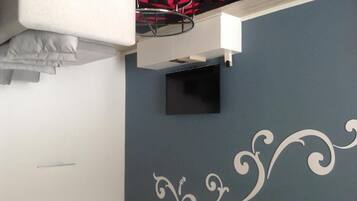A room with a blue wall, a white decorative pattern, a flat-screen TV mounted on the wall, and a white cabinet below it.