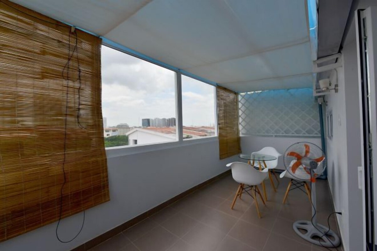 A balcony with a view of buildings, a table with chairs, and a fan.