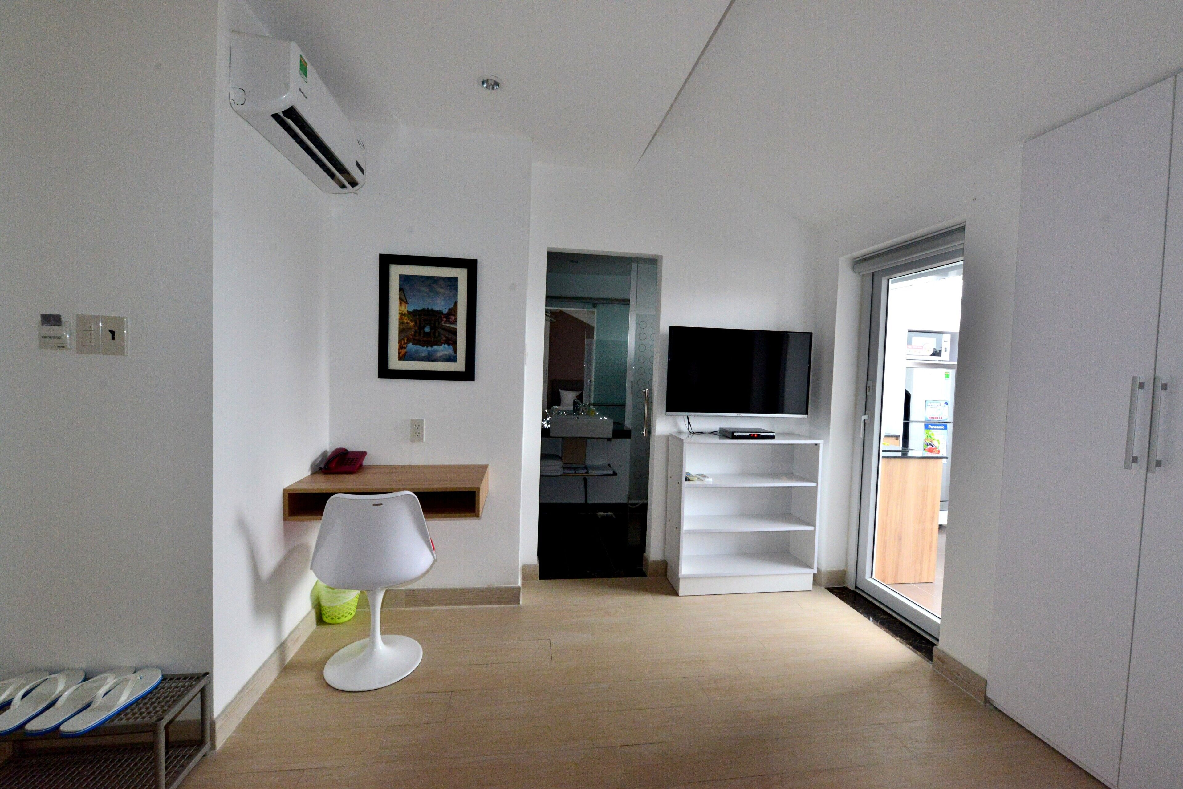 Quarto de hotel moderno com piso de madeira, luminária branca, televisão de tela plana e porta que dá para o banheiro.