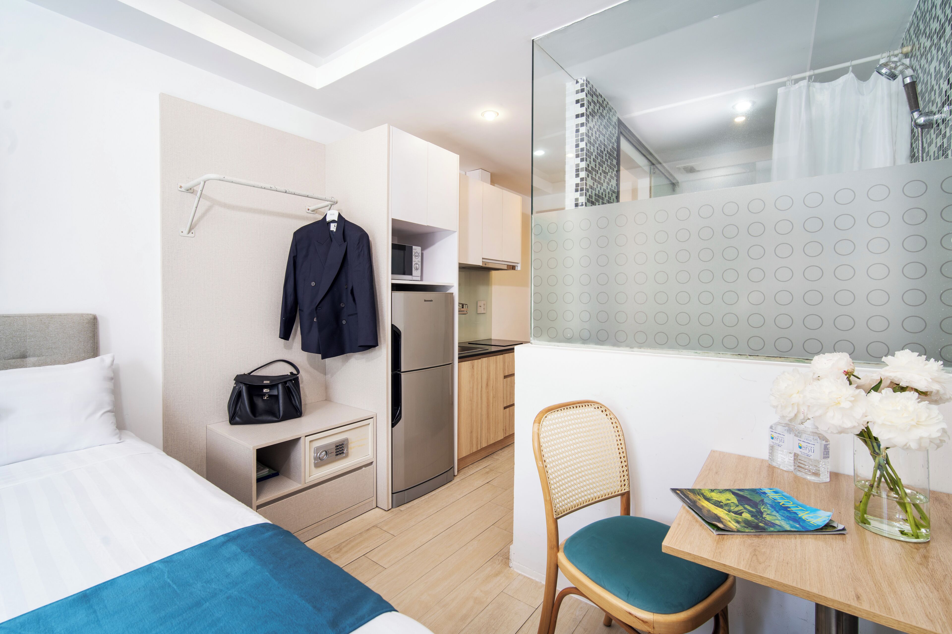 A hotel room with a bed, a desk with a chair, a small kitchenette, and a bathroom with a shower curtain.