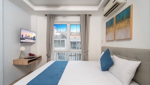 Une chambre d’hôtel avec un lit, une télévision, une fenêtre avec des rideaux et des œuvres d’art accrochées au mur.