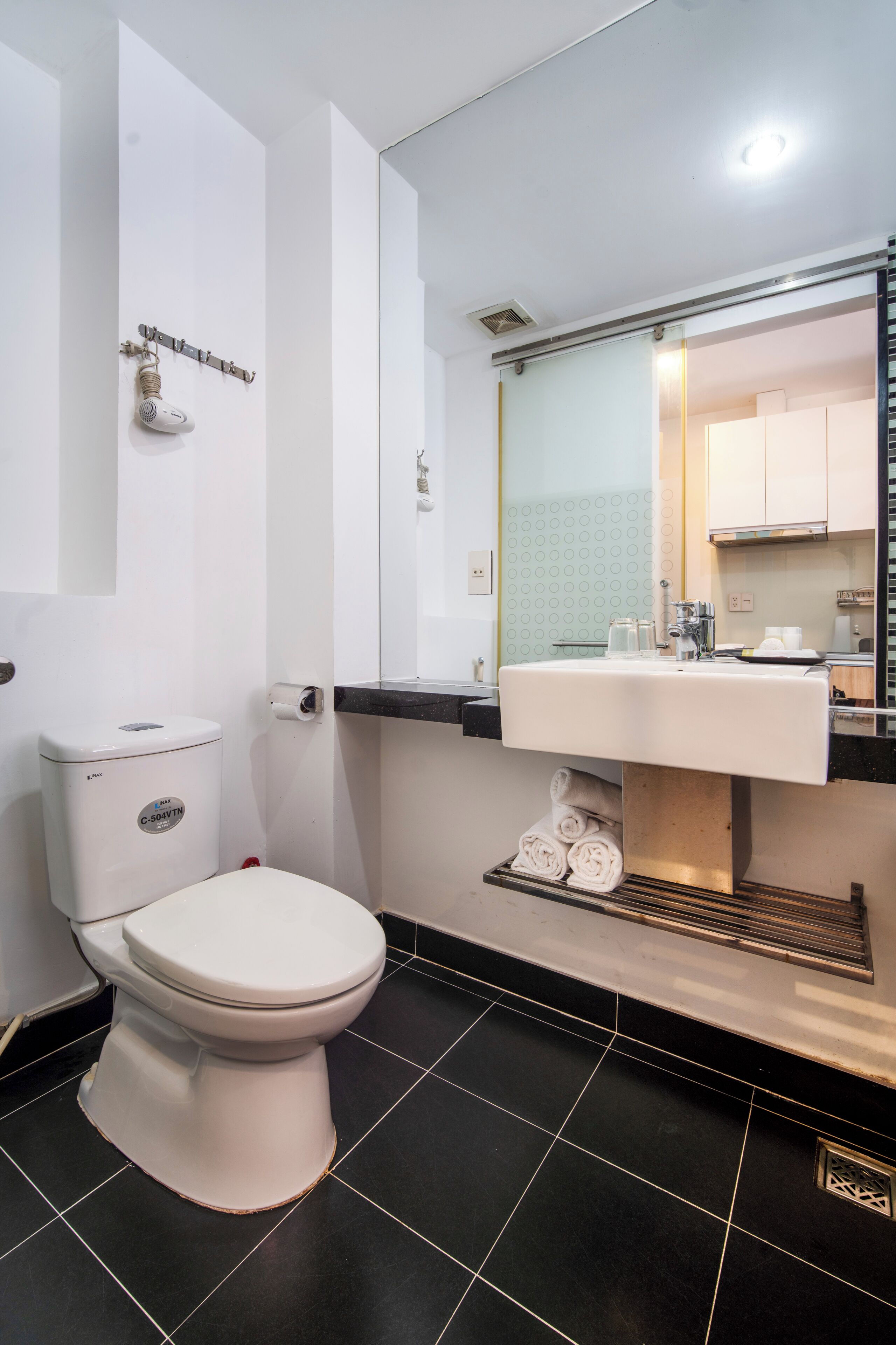 Un baño moderno con inodoro blanco, lavabo con espejo arriba y suelo de baldosas negras.