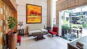Un hall d’entrée avec un grand tableau, un canapé, des fauteuils rouges, une table basse et une vue sur l’extérieur.