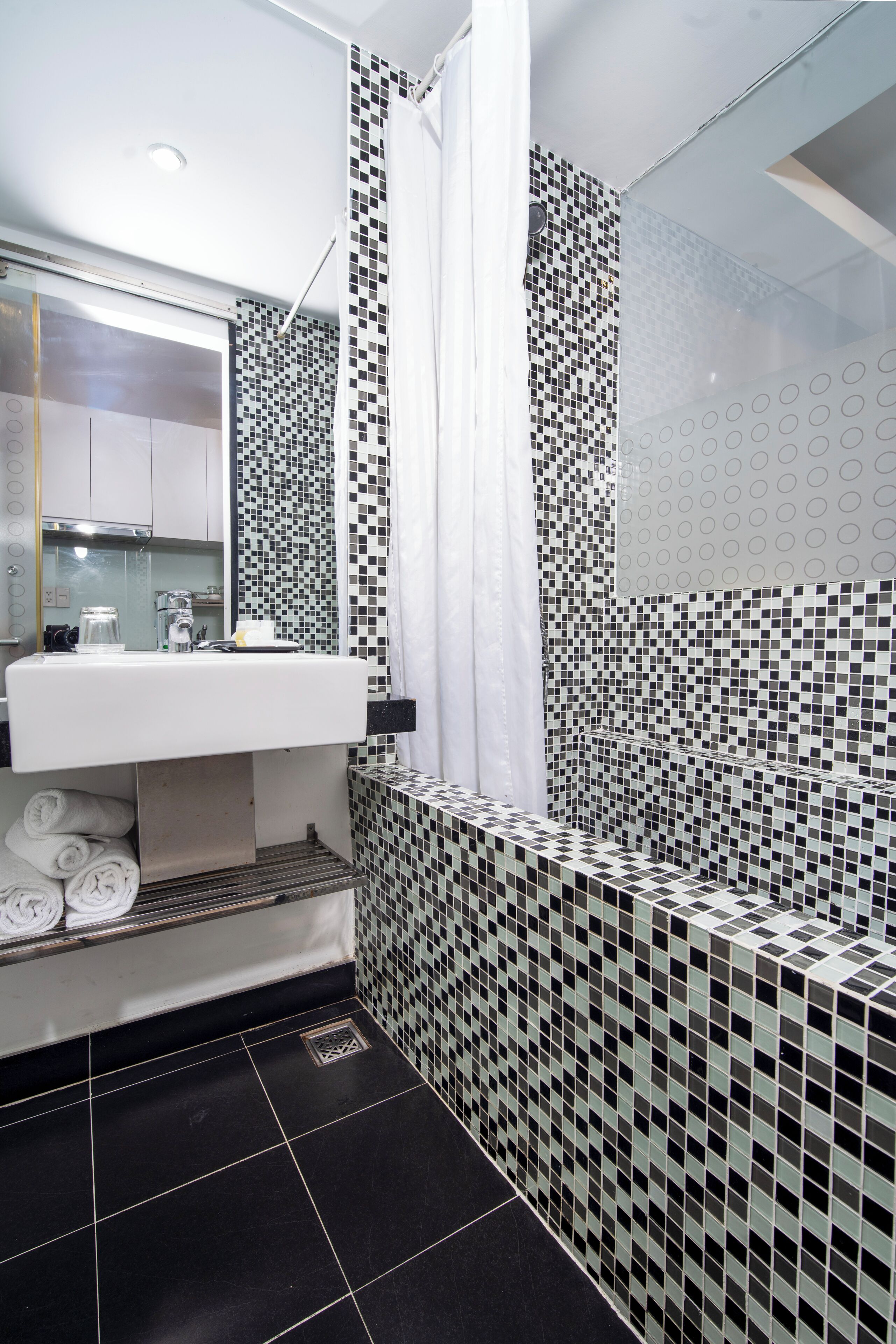 A modern bathroom with a white sink, black and white tiled walls, and a glass shower enclosure.