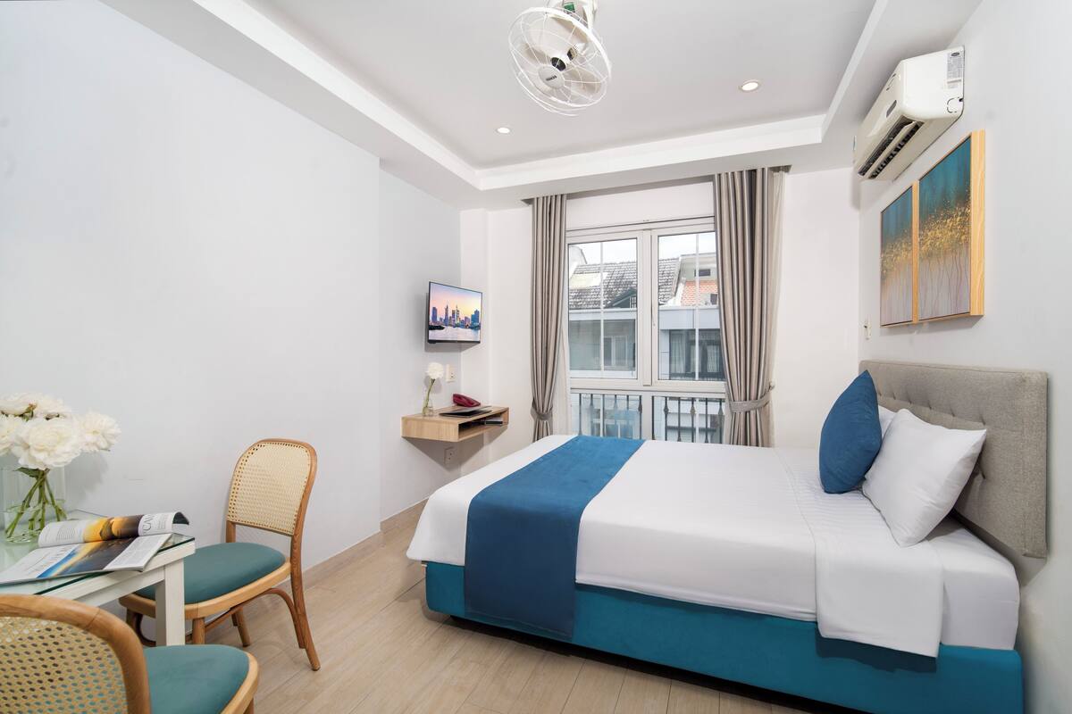 Hotellihuone, jossa on sänky, työpöytä tuolilla, televisio ja ikkuna, jossa on verhot.