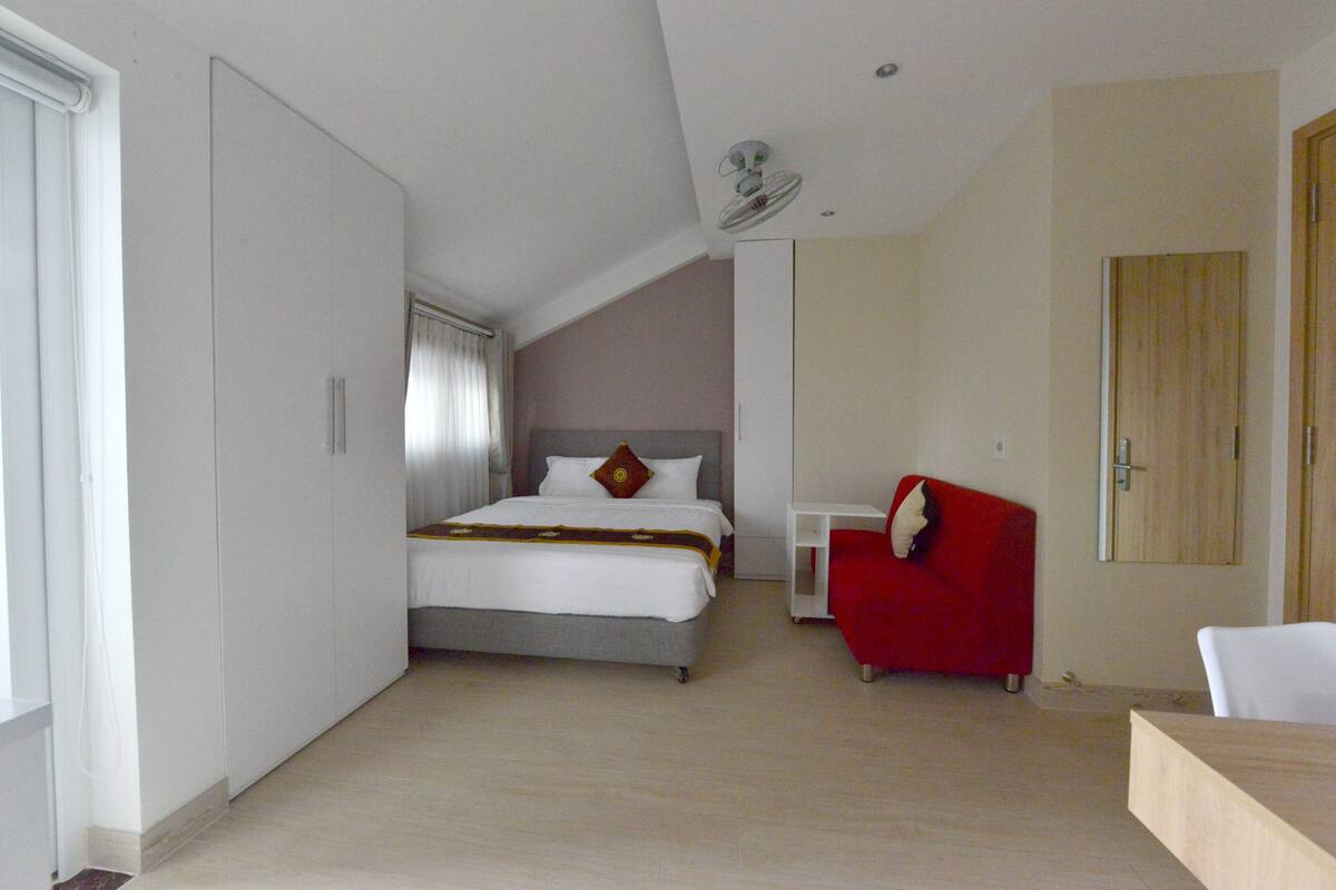 Hotellihuone, jossa on sänky, punainen tuoli, yöpöytä ja vaatekaappi.