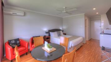Habitación de hotel con cama, escritorio, silla, mesa, ventilador de techo y kitchenette.