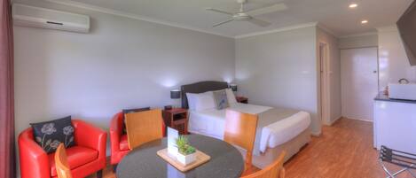 Habitación de hotel con cama, escritorio, silla, mesa, ventilador de techo y kitchenette.