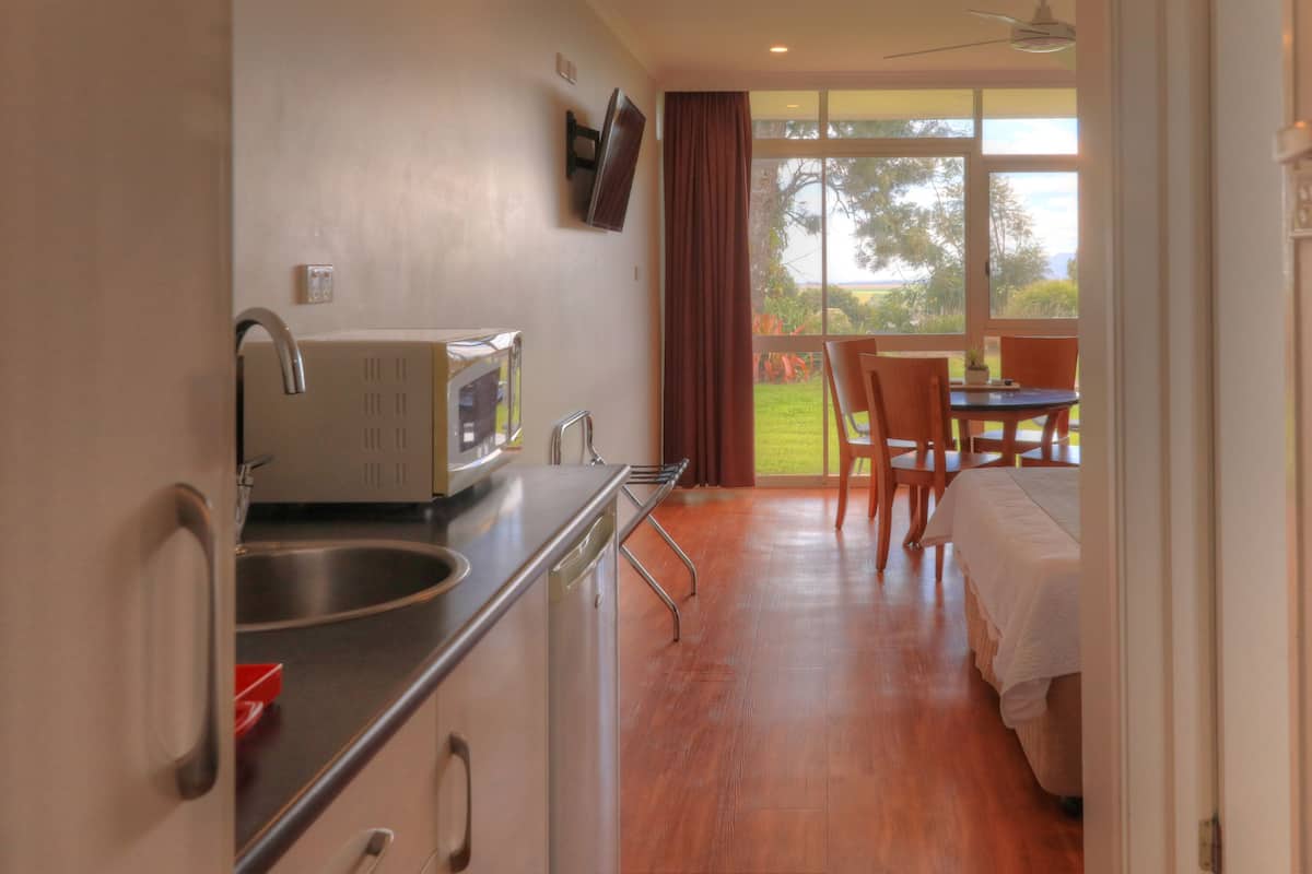 Cocina compacta con microondas, lavamanos y armarios, que da a un balcón con mesa y sillas.