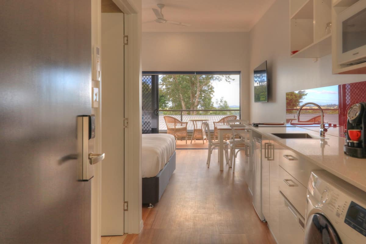 Cocina moderna con comedor, lavadora y un amplio ventanal con vistas a árboles.