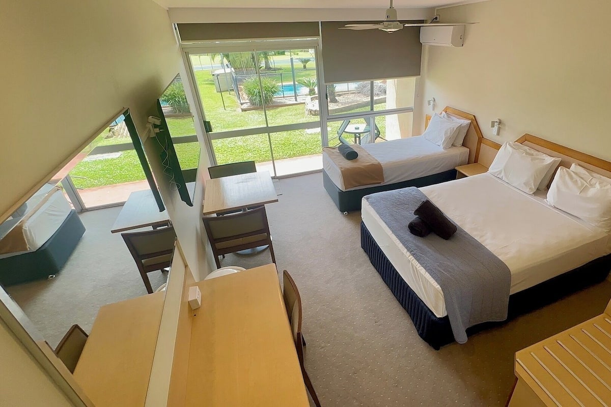 Habitación de hotel con dos camas, un escritorio, una silla y vistas a un jardín.