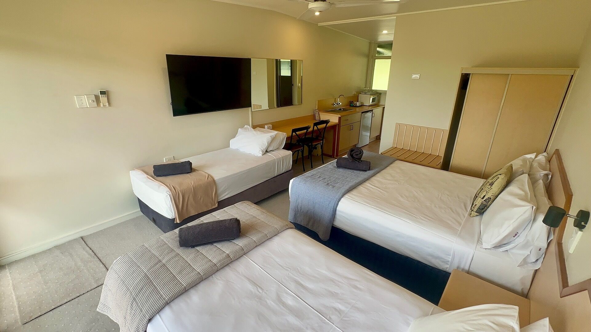 A hotel room with two beds, a TV, a mirror, a desk, and a kitchenette.