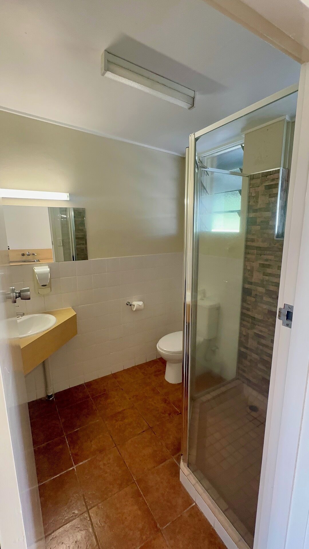 A bathroom with a shower, toilet, sink, and a mirror.