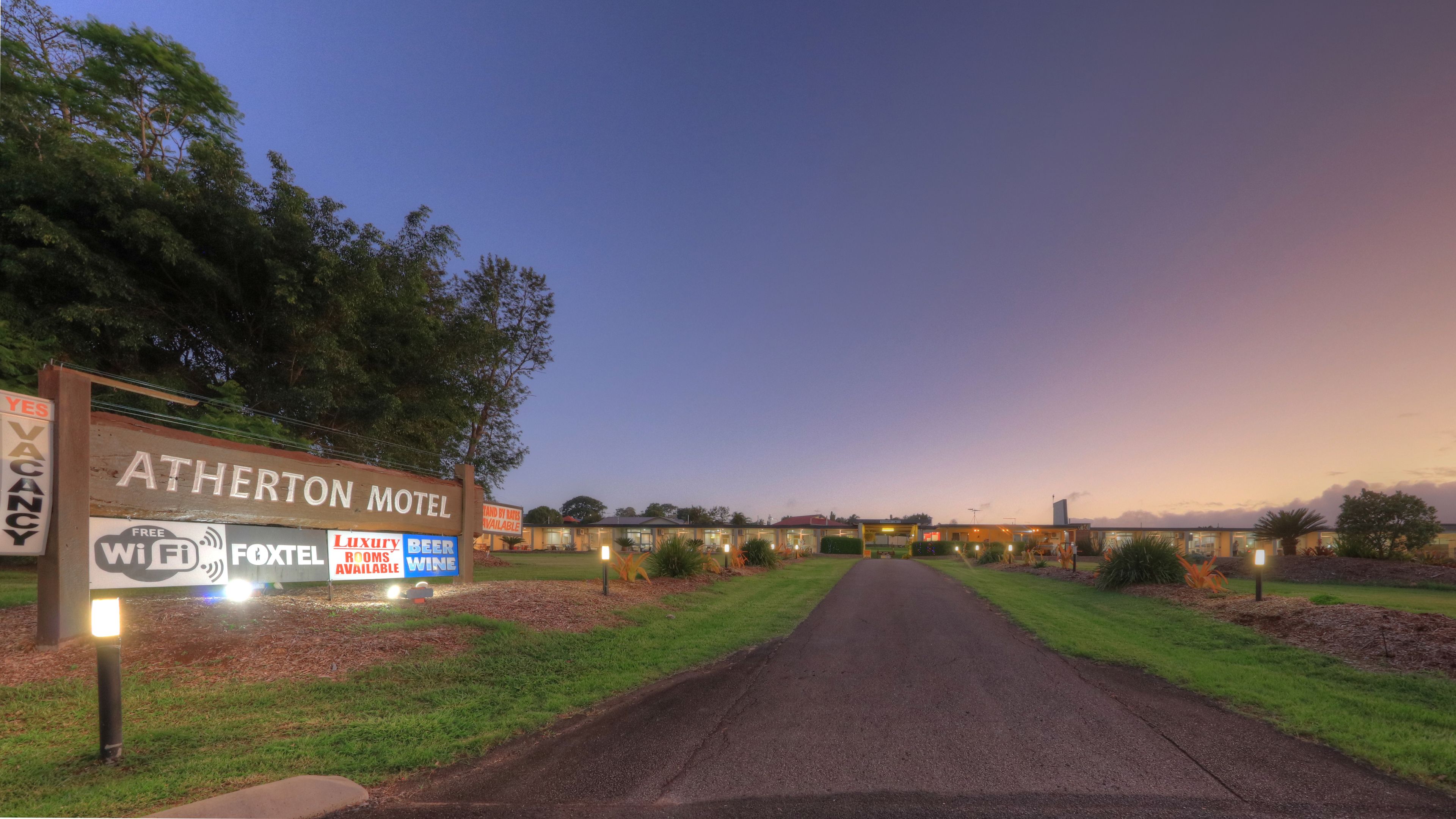 Het Atherton Motel met een bord waarop faciliteiten worden aangeboden, zoals gratis WiFi, FoxTel, luxe kamers en bier en wijn.