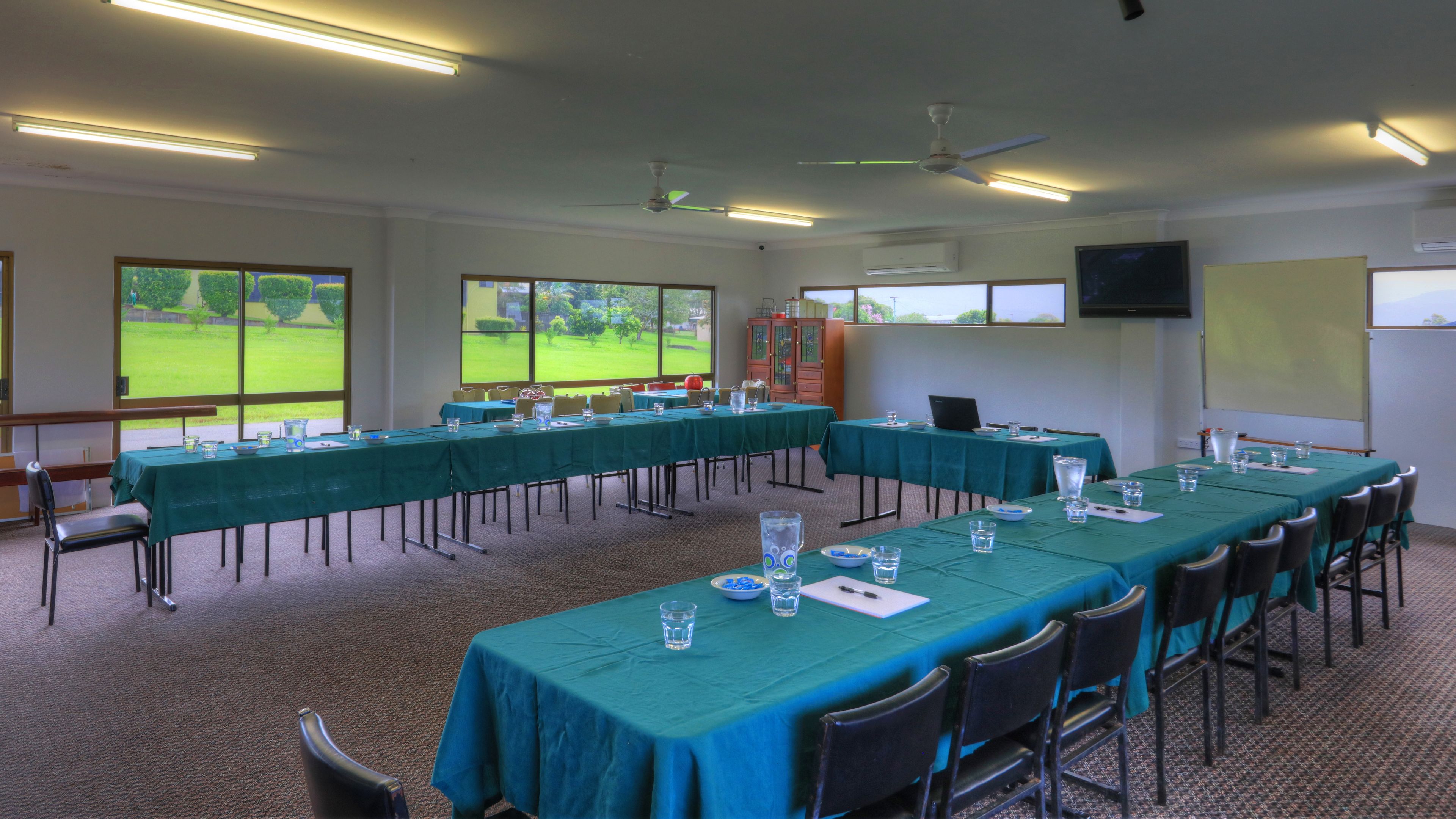 A conference room with long tables, chairs, and a projector screen.